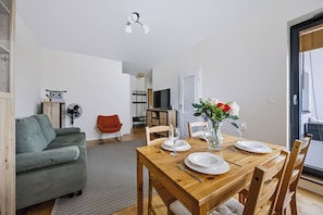 A dining area with a wooden table set for four, a grey sofa, a red chair, and a vase with flowers. - Warsaw Urban Wola Apt — Parking & Balcony (Warsaw)