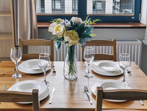 A dining table set for four with white plates, cutlery, and wine glasses, centered with a vase of flowers. - Warsaw Urban Wola Apt — Parking & Balcony (Warsaw)
