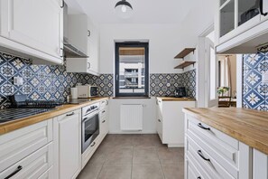 A compact kitchen with white cabinets, a central island, and patterned backsplash tiles. - Warsaw Urban Wola Apt — Parking & Balcony (Warsaw)