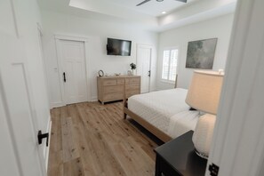 Quarto com cama, penteadeira, televisão e janela com persianas.