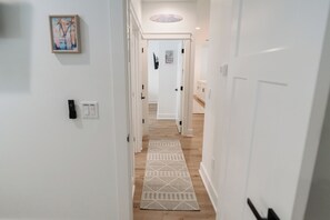 Un couloir aux murs blancs, orné d’un tapis à motifs et doté d’une porte donnant sur une pièce au plancher en bois.