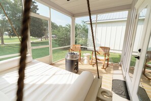 A bedroom with a bed, a heater, and a view of a grassy area through large windows. - Lavender Landing - Family Coastal Family Getaway Near Gulf Shores & OWA (Foley)