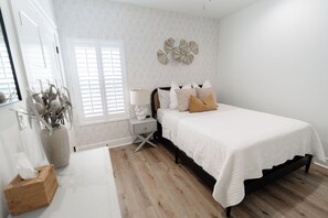A bedroom with a bed, bedside table, lamp, and decorative wall piece. - Lavender Landing - Family Coastal Family Getaway Near Gulf Shores & OWA (Foley)
