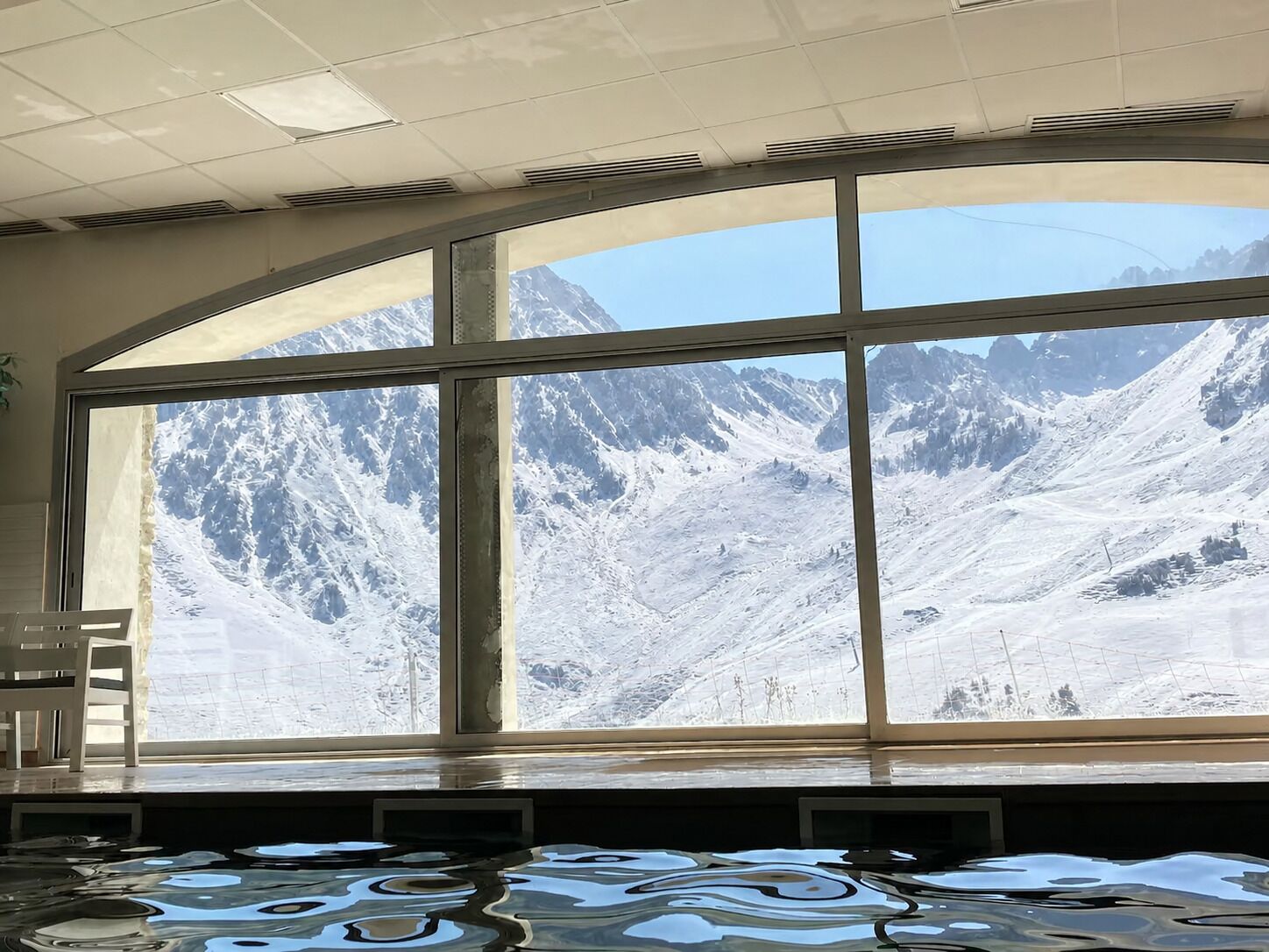 A room with a large arched window offering a view of snow-covered mountains.