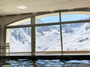 A room with a large arched window offering a view of snow-covered mountains. - Studio La Mongie- Moderne et cosy avec vue sur les pites et piscine (Bagnères-de-Bigorre)