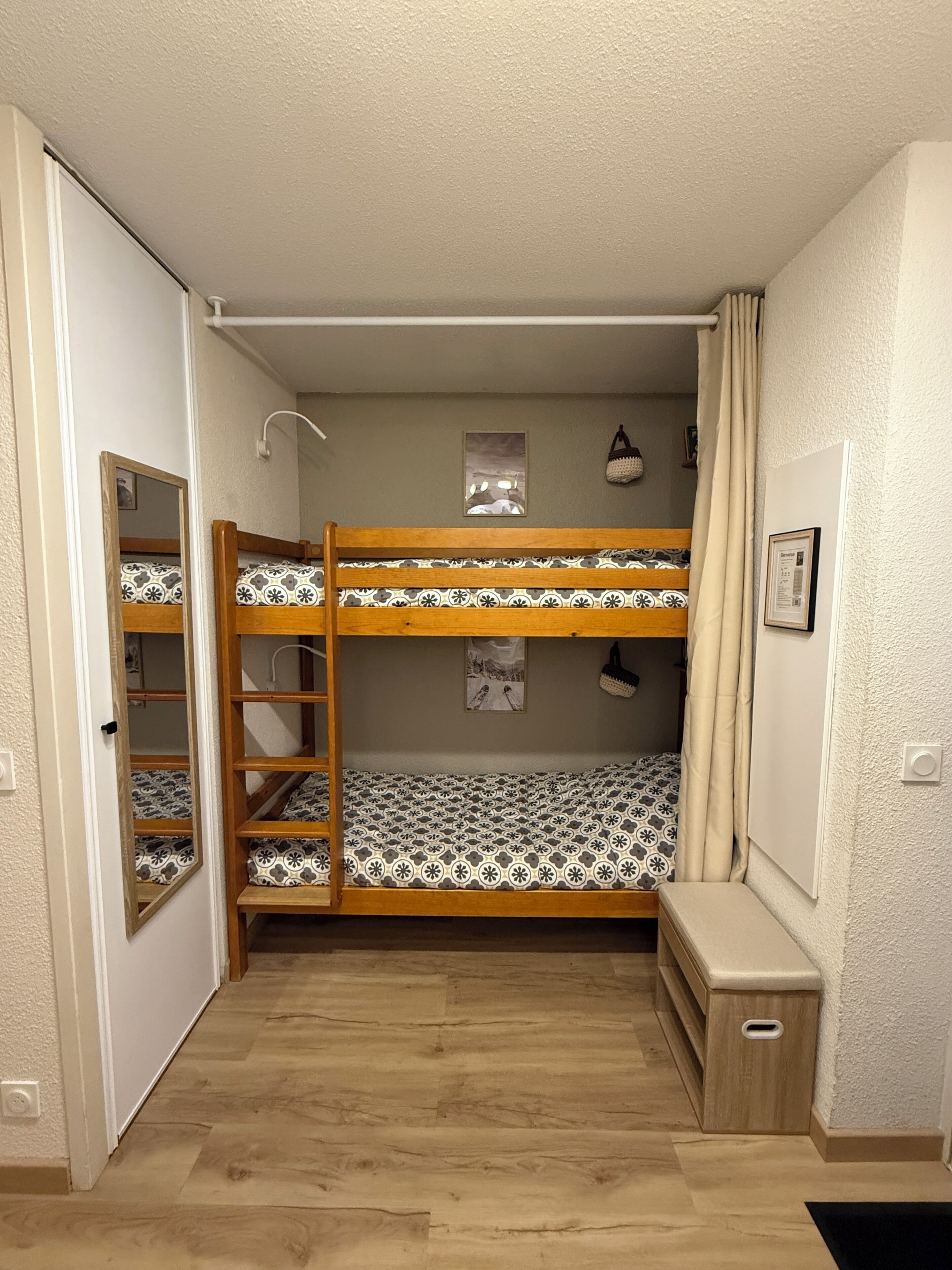 Dormitorio con literas, una escalera de madera, un pequeño banco y un estante en la pared.