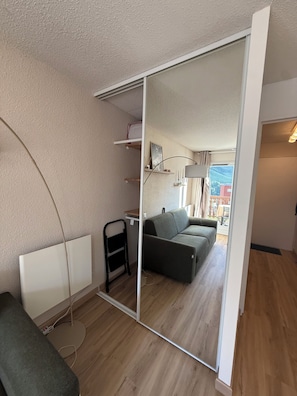 A room with a sliding glass door leading to a balcony, a grey sofa, a small table, and a lamp. - Studio La Mongie- Moderne et cosy avec vue sur les pites et piscine (Bagnères-de-Bigorre)