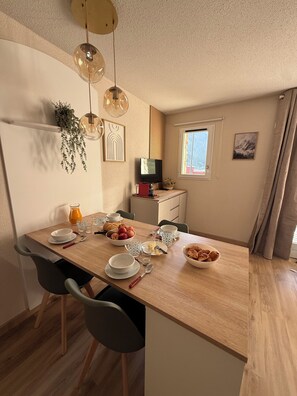 A dining area with a wooden table, chairs, and a television. - Studio La Mongie- Moderne et cosy avec vue sur les pites et piscine (Bagnères-de-Bigorre)