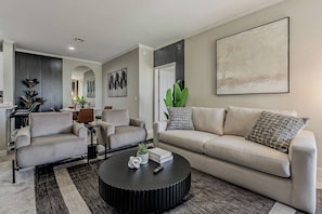 Uma sala de estar moderna com sofá, duas poltronas, uma mesinha de centro e um espaço de jantar com cadeiras e mesa.