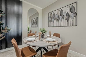 Uma área de jantar com mesa redonda posta para seis pessoas, rodeada por seis cadeiras marrons.