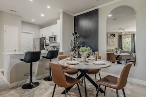 A modern dining area with a round table, chairs, and a kitchen in the background.