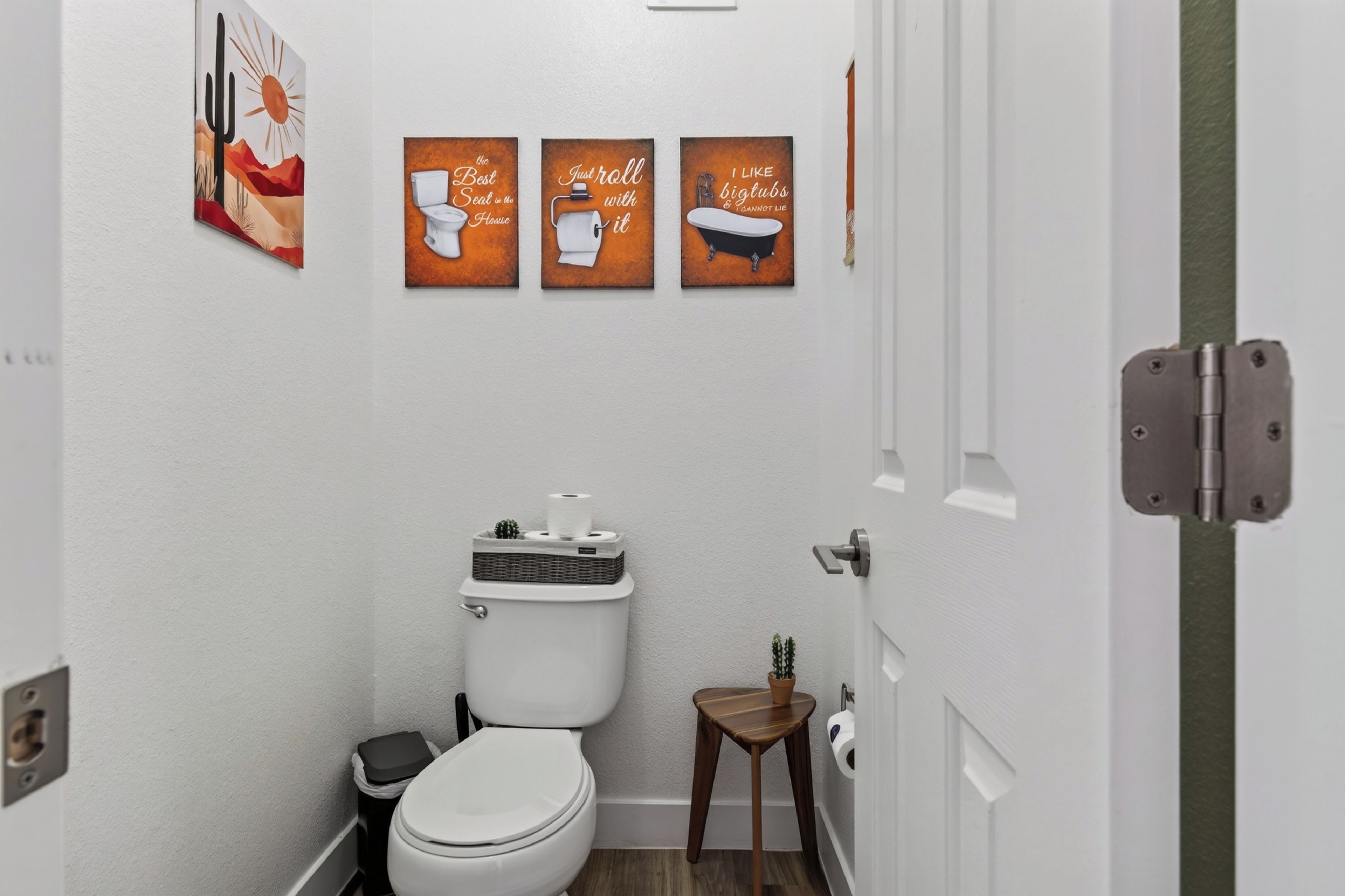 A small, modern bathroom with a toilet, a small wooden stool, and three wall-mounted signs.
