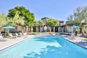 A swimming pool with lounge chairs and umbrellas, surrounded by trees and buildings.