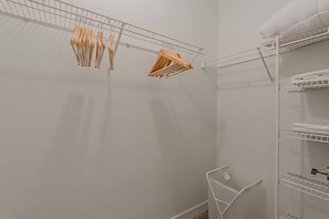 A room with a white wall, a metal drying rack, and a white shelf unit with folded towels.