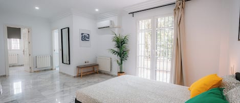 Un dormitorio con una cama, un banco, una planta en maceta y un ventanal con cortinas.