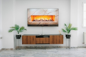 A modern living room with a flat-screen TV mounted above a wooden console table, flanked by two floor-standing speakers and potted plants. - Villa Zarra, Granada (Maracena)