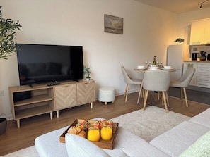 A modern living room with a flat-screen TV, a dining area with a table set for two, and a kitchen in the background. - Stylish Central Warrington Stay | Free Parking (Warrington)