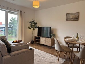 A modern living room with a sofa, a dining table set for two, a television, and a potted plant. - Stylish Central Warrington Stay | Free Parking (Warrington)
