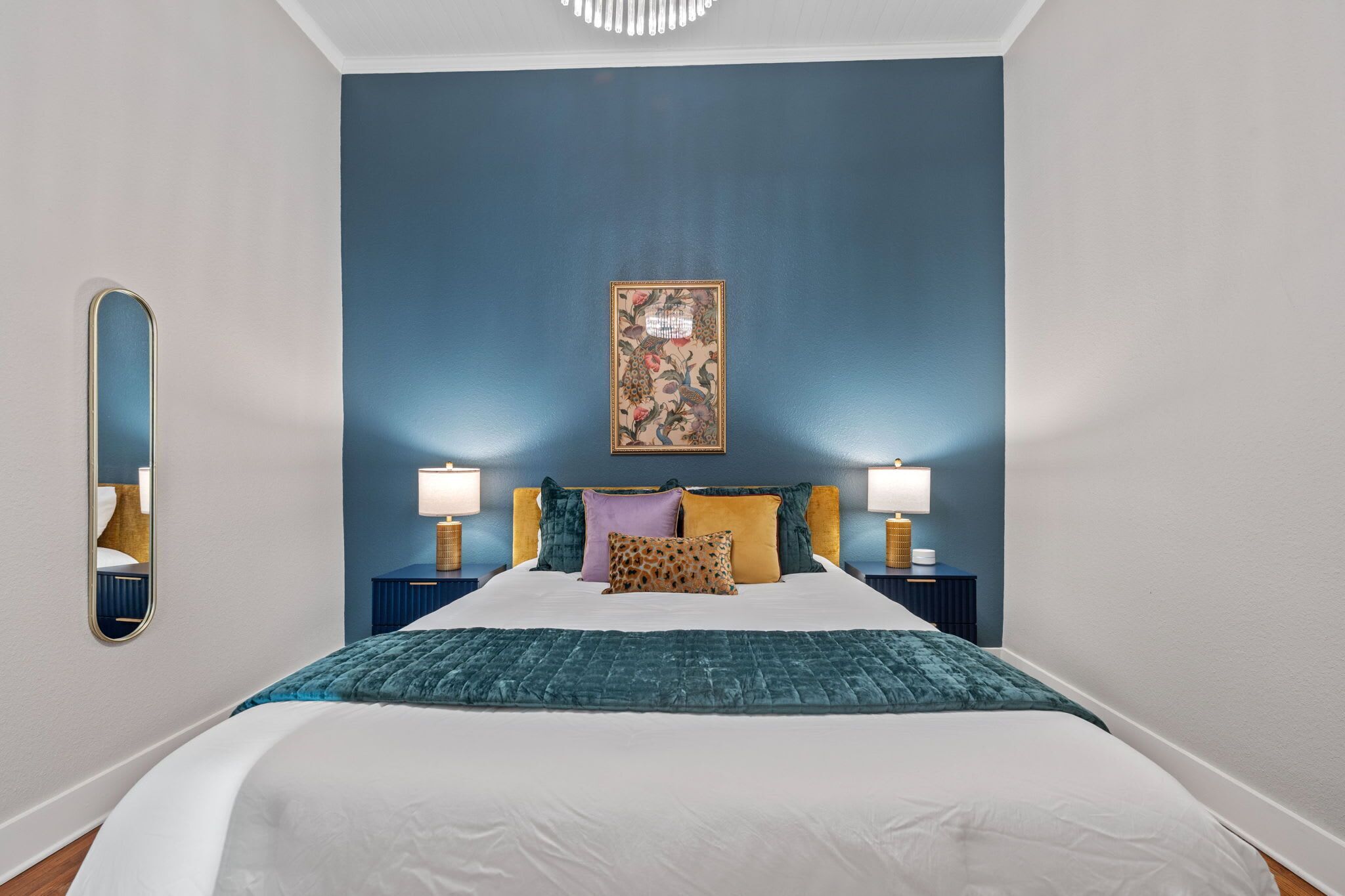 A bedroom with a large bed, two bedside tables, a mirror, and a wall-mounted picture.