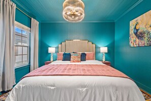 Une chambre à coucher avec un grand lit, deux tables de chevet avec des lampes, un lustre et un tableau au mur.