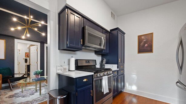 A modern kitchen with dark cabinetry, stainless steel appliances, and a marble countertop.