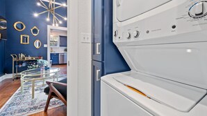 A modern kitchen with blue walls, a chandelier, and a dining area with a glass table and chairs.