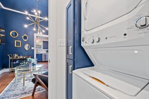 Une cuisine moderne aux murs bleus, agrémentée d’un lustre et comprenant un coin repas avec une table et des chaises en verre.