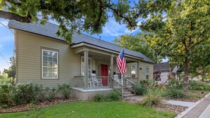 A single-story house with a front porch, a red door, and an American flag.