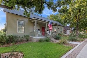 Une maison de plain-pied avec un porche à l’avant, une porte rouge et un drapeau américain.