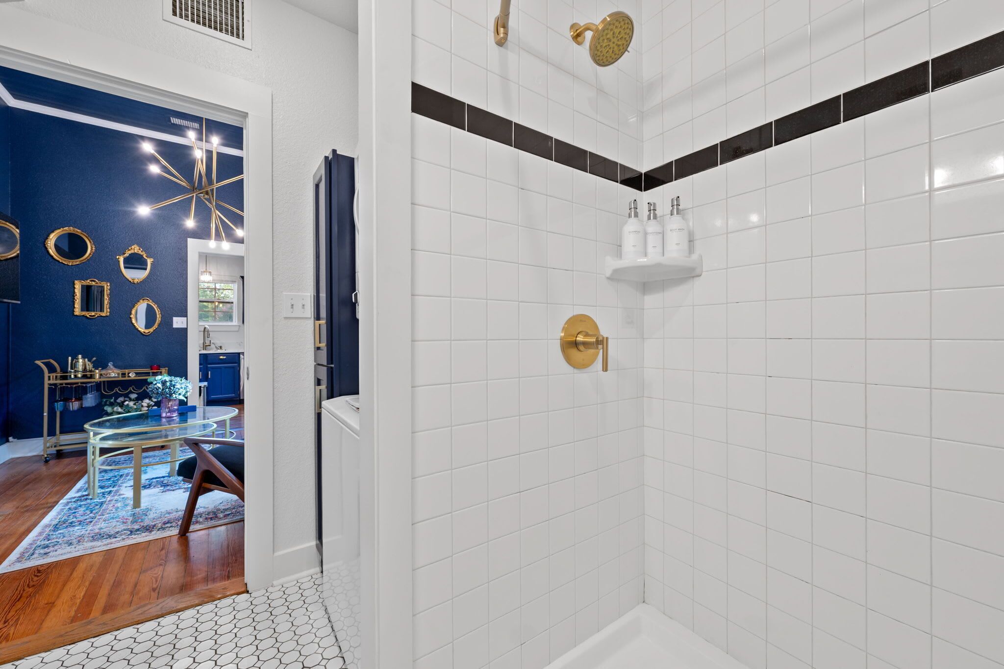 A modern bathroom with white tiles, a shower with a gold faucet, and a visible toilet paper holder.