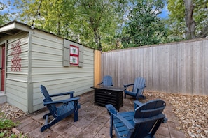 Un área de patio con sillas Adirondack y una mesa, un cobertizo con contraventanas decorativas y una valla de madera.