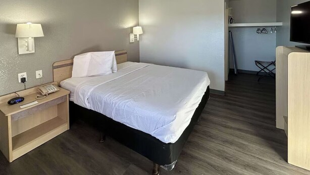 A hotel room with a bed, bedside lamps, a desk with a phone, and a TV. - Budget-Friendly Stay with Kitchen + Free Parking | Maxey Park - 0.7 mile (Lubbock)