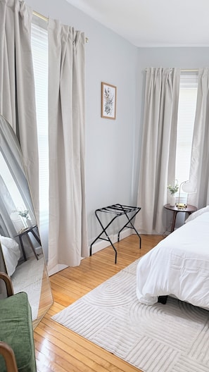 A bedroom with a bed, a side table, a mirror, and a window with curtains. - Cozy Modern Oasis near Kelley Square (Worcester)