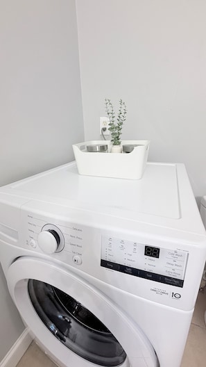 A front-loading washing machine with a control panel and a small plant on top. - Cozy Modern Oasis near Kelley Square (Worcester)