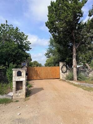 Ein Schotterweg führt zu einem Holztor mit einem Steinsammlerschrank und einer Mauer mit einer Hausnummer.