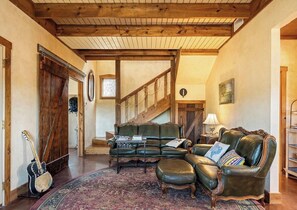 Ein gemütliches Wohnzimmer mit einer Ledersofa, einem Couchtisch und einer Gitarre. Eine Treppe mit Holzwandungen führt eine weitere Ebene hinauf.