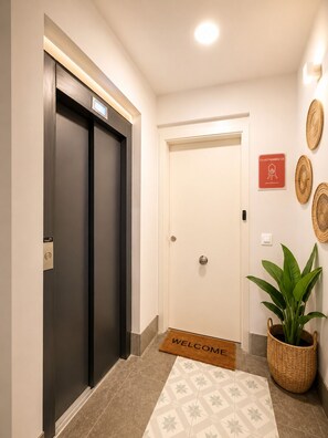 Een hotelentree met een receptiebalie, een welkomstmat, een potplant en een bord dat aan de muur hangt.