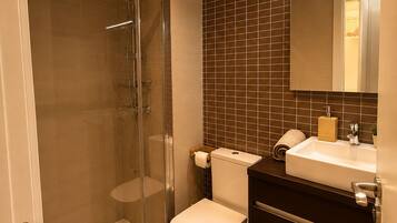 Baño con ducha envuelta en vidrio, inodoro y lavamanos con espejo.