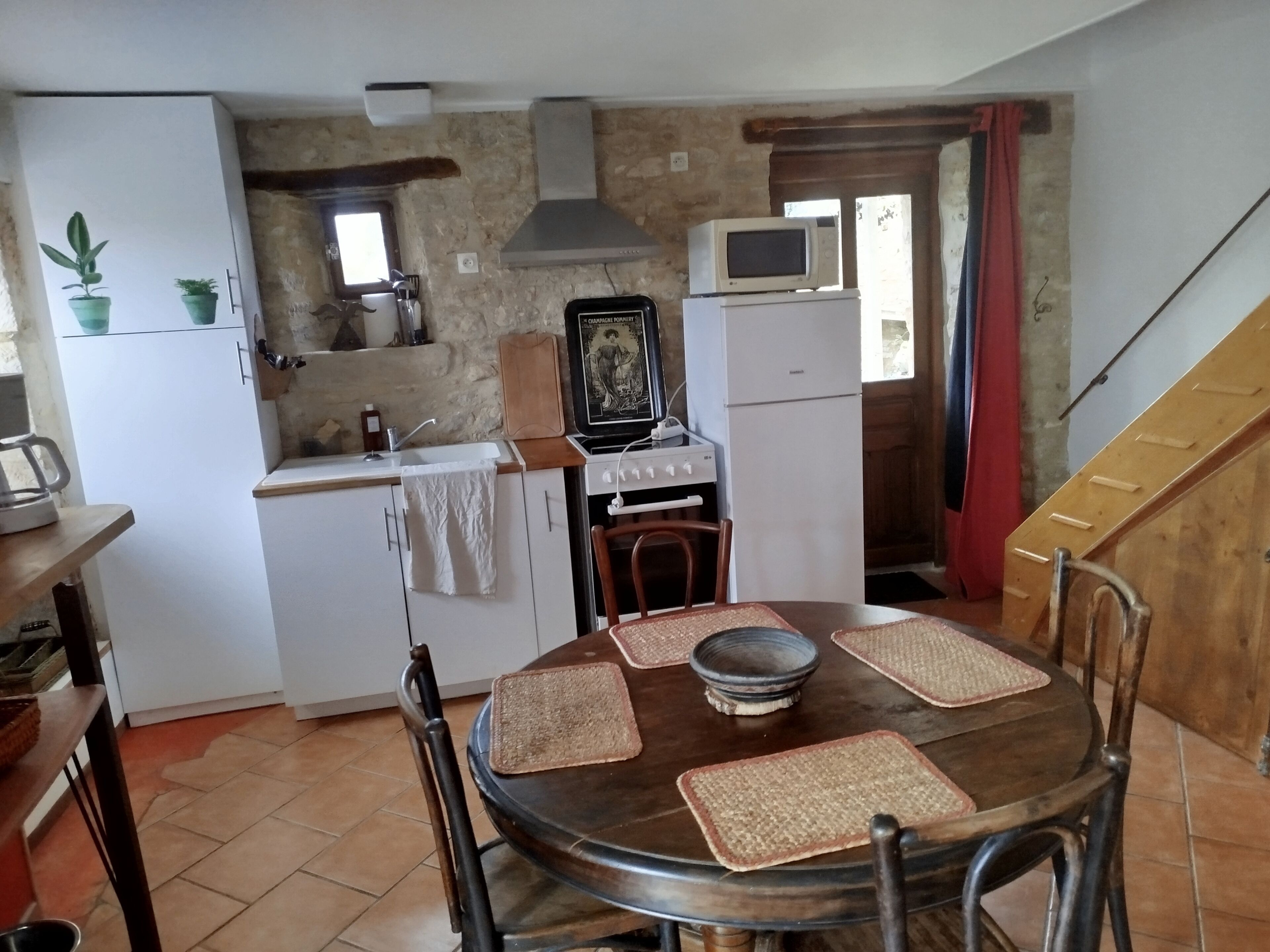Une cuisine compacte équipée d’une cuisinière, d’un four à micro-ondes et d’un réfrigérateur. On y trouve une table à manger avec des chaises et des sets de table.