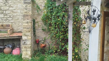 Un mur de pedra rústic amb una porta de fusta, una petita zona de jardí amb gespa i plantes, i una bicicleta adossada a la paret.