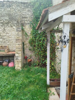 A rustic stone wall with a wooden door, a small garden area with grass and plants, and a bicycle leaning against the wall.