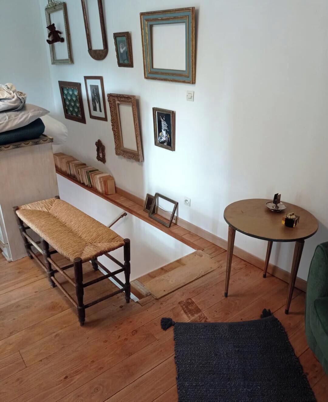 Een kamer met een bankje, een klein tafeltje en een plank vol boeken.