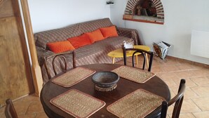 Un comedor con una mesa redonda, sillas y un sofá con cojines anaranjados.
