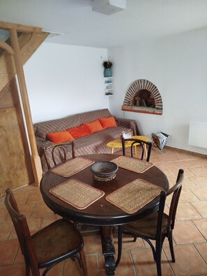 Een eethoek met een ronde tafel, stoelen en een bank met oranje kussens.