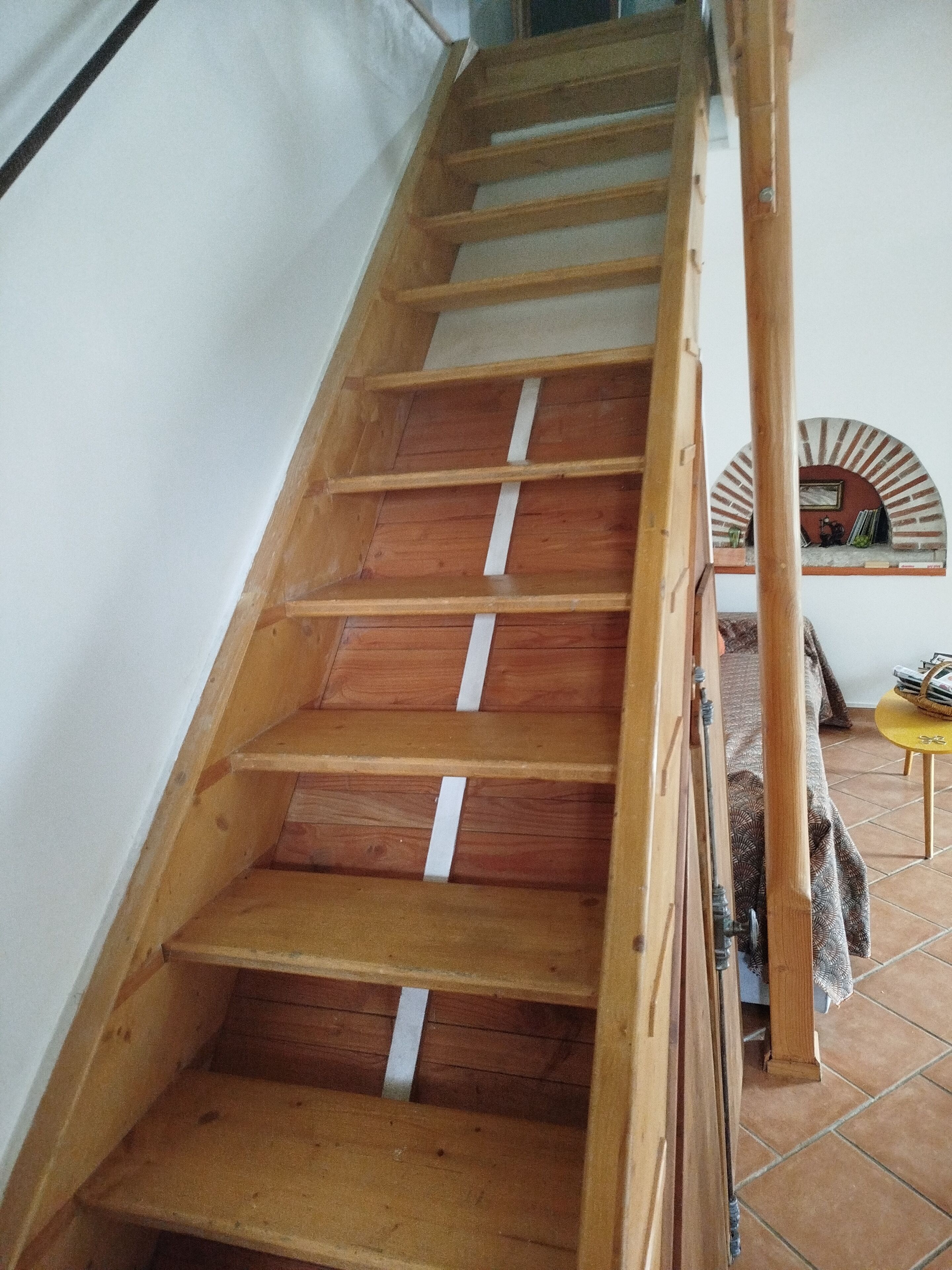 Een houten trap met witte treden, die uitkomt op een overloop met een klein tafeltje en een decoratieve spiegel.
