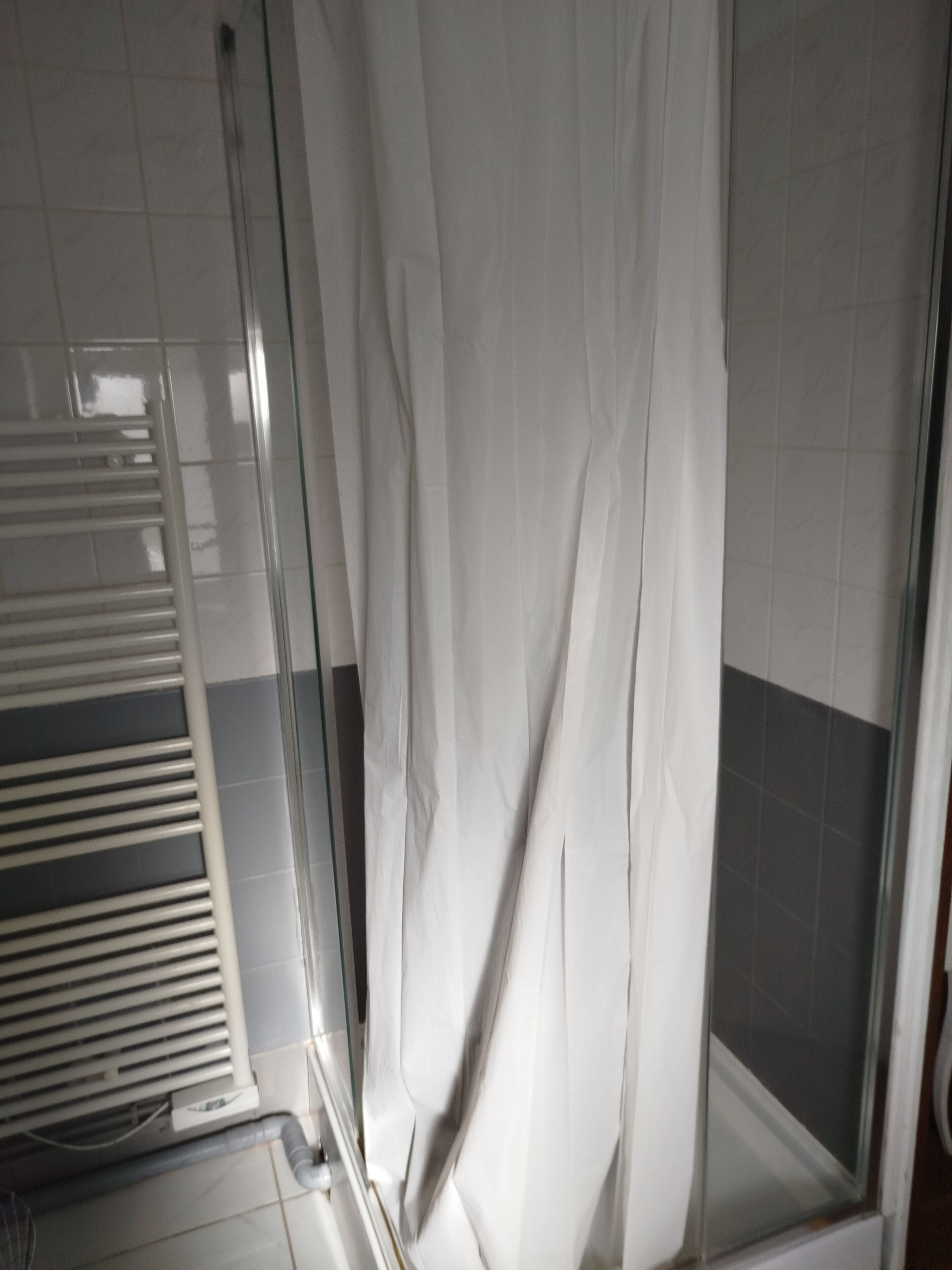 A bathroom with a glass shower enclosure, a white towel rack, and tiled walls.