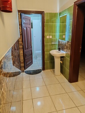 A bathroom with a white sink, green tiled walls, a brown door, and a tiled floor. - Khairjewar Ap1st Floor 4bedroom (Madinah)