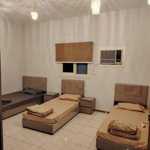 A room with two beds, a window with blinds, an air conditioning unit, and a bedside table with a lamp. - Khairjewar Ap1st Floor 4bedroom (Madinah)