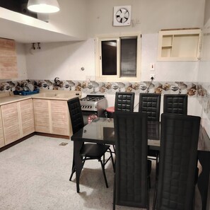 A compact kitchen with a gas stove, a window, and a dining area with four chairs. - Khairjewar Ap1st Floor 4bedroom (Madinah)