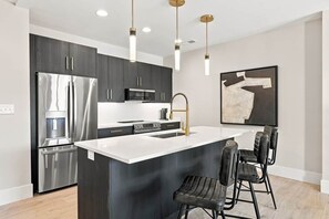 Una cocina moderna con armarios oscuros, electrodomésticos de acero inoxidable, una isla con encimera blanca y un taburete de bar.